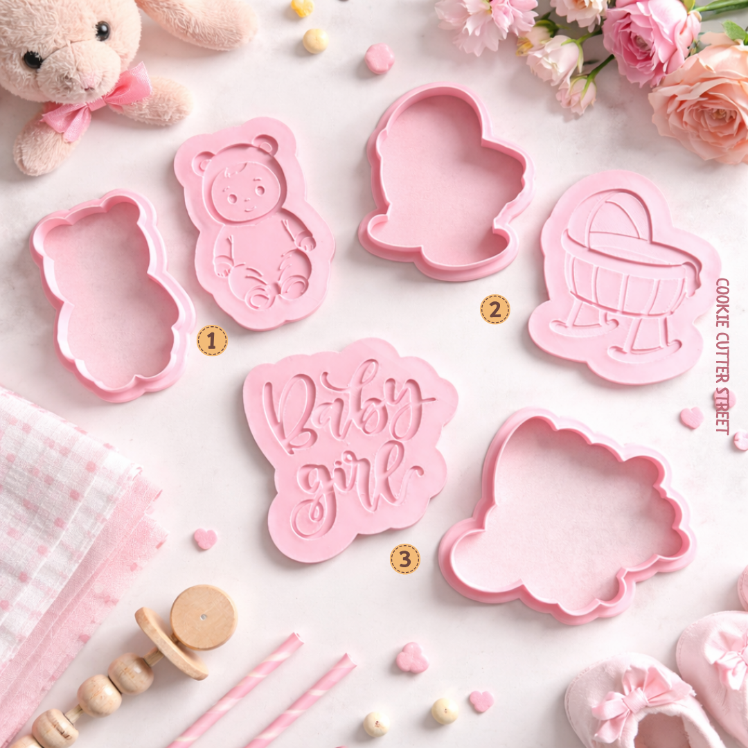 Set of pink cookie cutters with baby-themed designs on a white surface with decorative items.