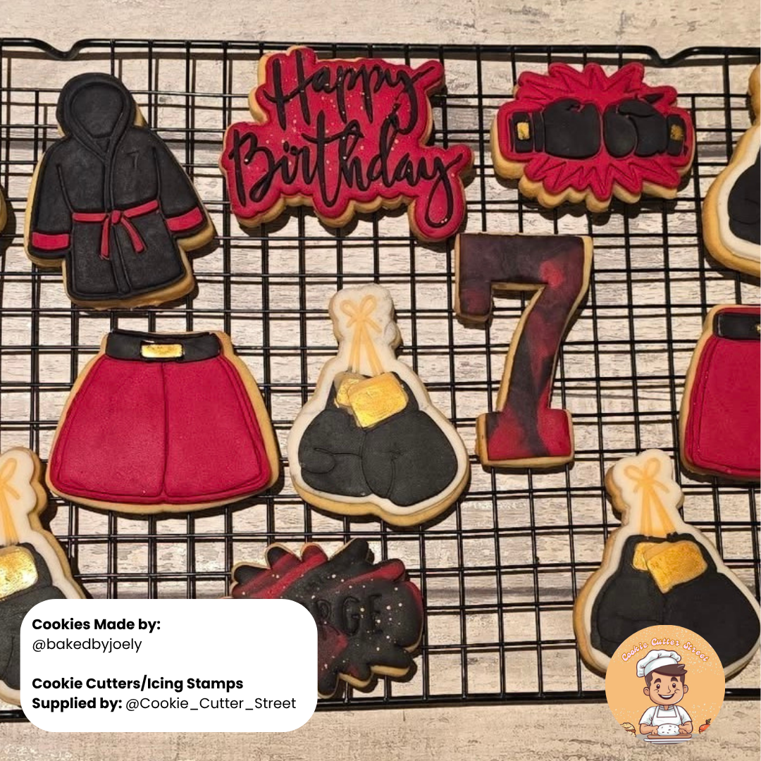Decorative boxing themed cookies shaped like a robe, gloves and number 7 on a cooling rack with 'Happy Birthday' text.