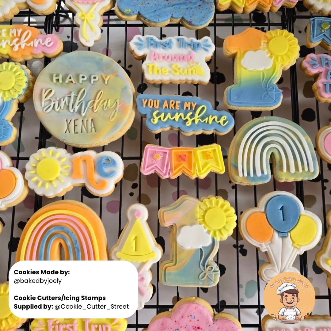 Decorative cookies with text and designs on a cooling rack, made by @bakedbyjoely.