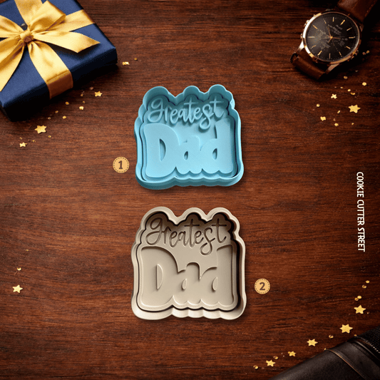 Two cookie cutters with 'Greatest Dad' text on a wooden surface with a gift and watch.