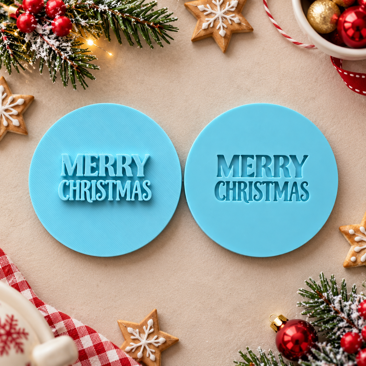 Two round light blue cookie cutters with raised 'MERRY CHRISTMAS' text, shown on a beige surface with Christmas decorations around them.