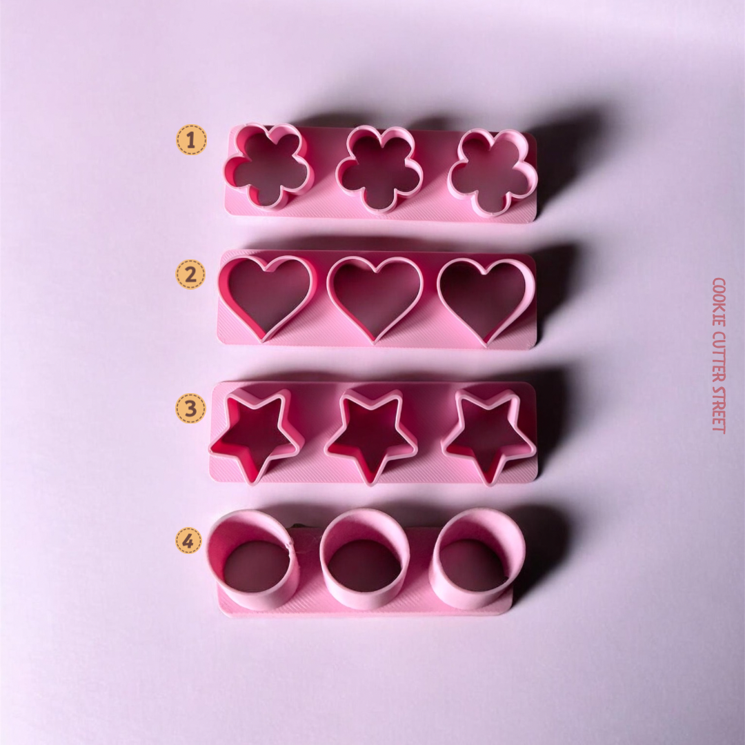 Set of pink cookie cutters with different shapes on a light purple background.