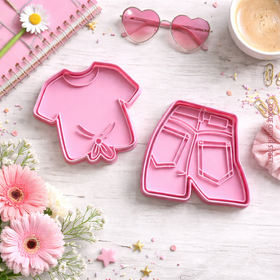Pink cookie cutters with imprint stamps shaped like a T-shirt and denim jeans on a styled pastel background.
