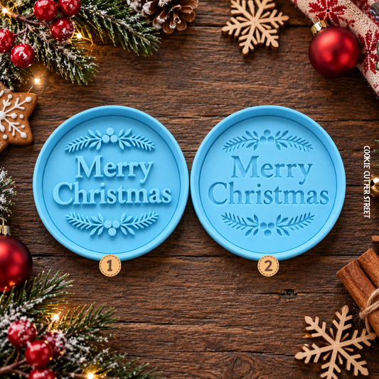 Two round light blue Christmas ornament. Ollie. Utter icing stamps with 'Merry Christmas' embossed in the center, displayed on a rustic wooden background surrounded by holiday decorations including pine branches, red ornaments, cinnamon sticks, and wooden snowflakes.