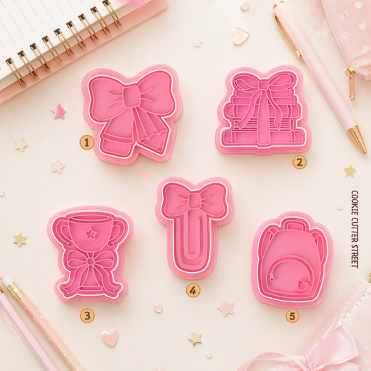 School-themed cookie stamp and cutter set featuring cute bow-inspired designs including school pencil, books, a trophy, a paperclip and a backpack.